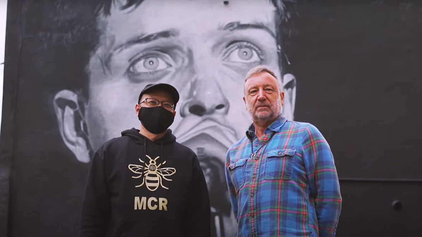 Der Streetart-Künstler Akse P19 und Joy Division-Bassist Peter Hook vor dem Ian Curtis-Wandbild in Manchester
